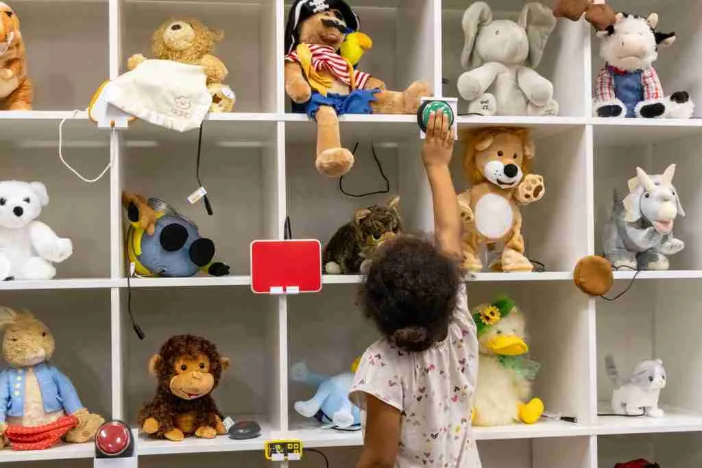 A child reaches for a stuffed animal on a shelf filled with various plush toys, promoting interactive play and exploration.