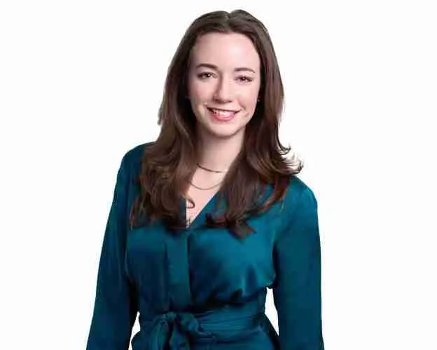 Smiling woman in a teal blouse with long hair, posing confidently against a white background.